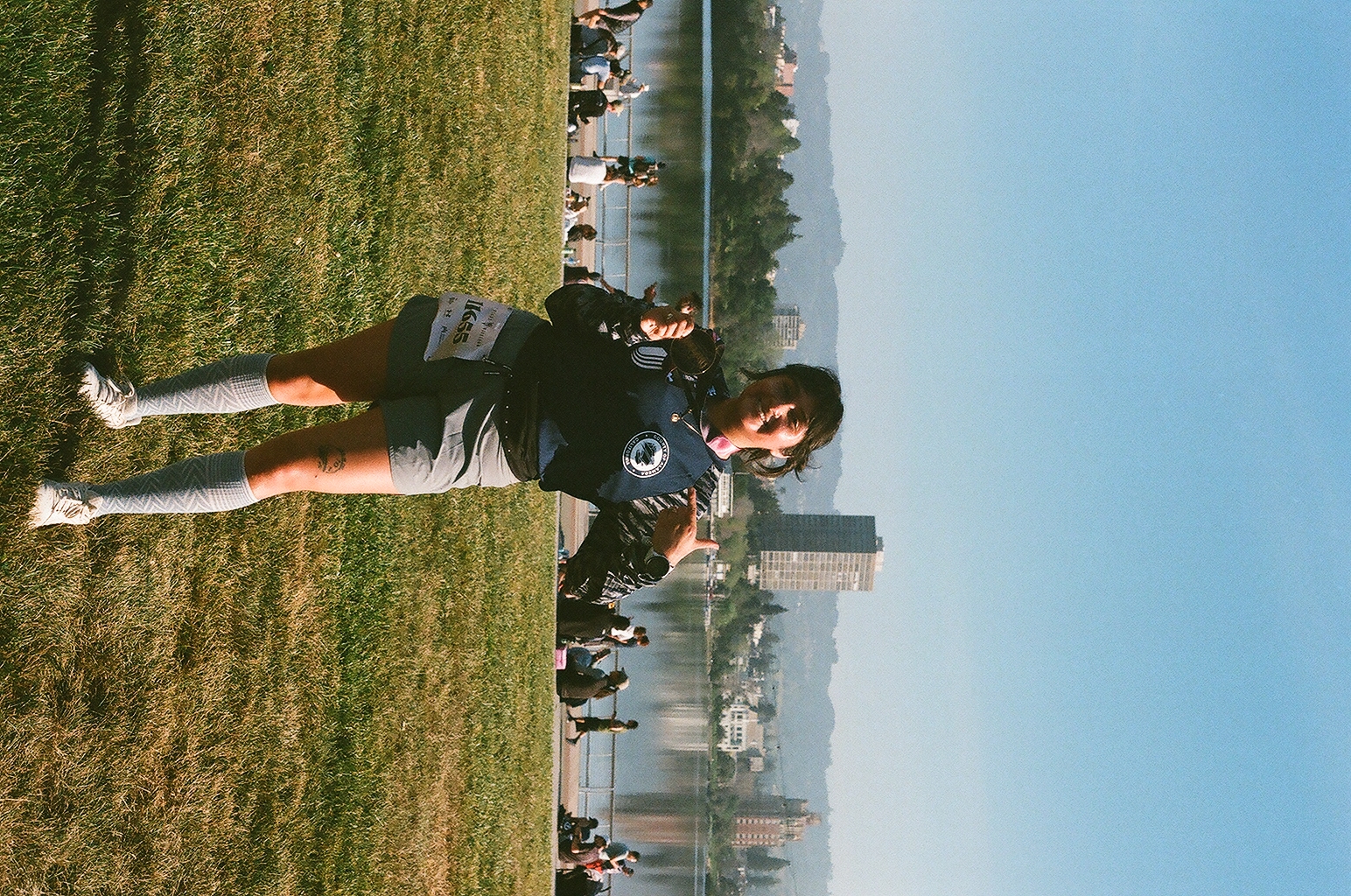 A runner in knee socks holds up her finisher's medal on the lawn at Lake Merritt