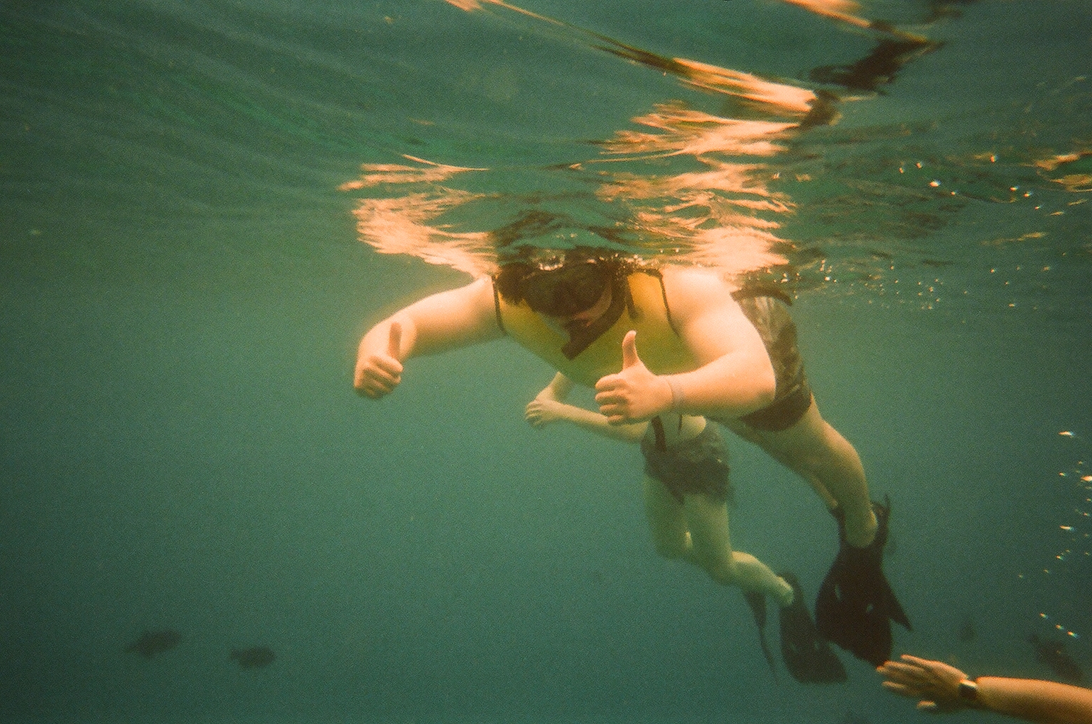 Snorkeler in a yellow vest and mask giving two thumbs up underwater
